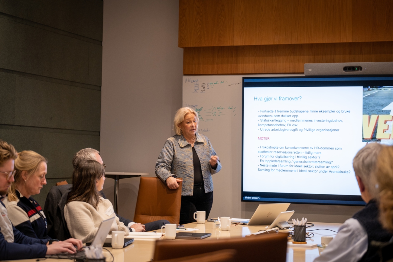 En dame står og presenterer for noen mennesker i et møterom.