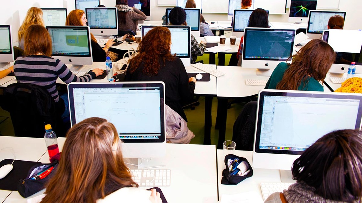 Studenter som sitter i et klasserom med hver sin PC eller Mac