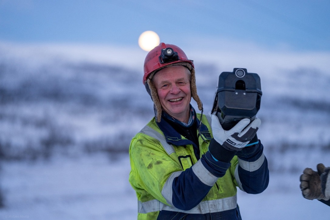 Mann med arbeidsutstyr står ute i vinterlige omgivelser og holder oppe et overvåkningsprodukt.