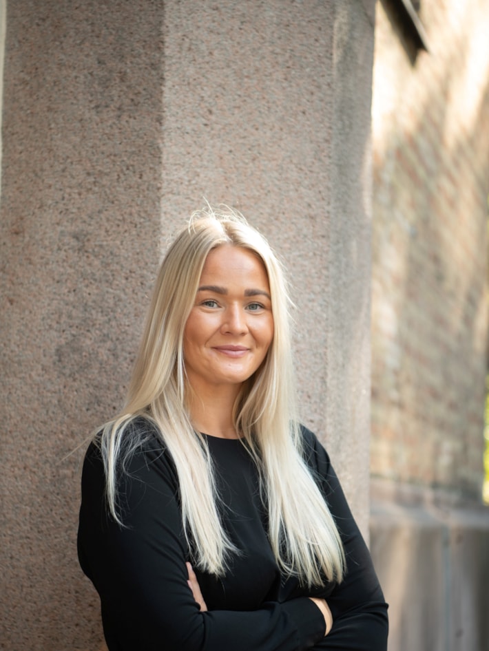 En dame har hendene i kryss og smiler til kamera.